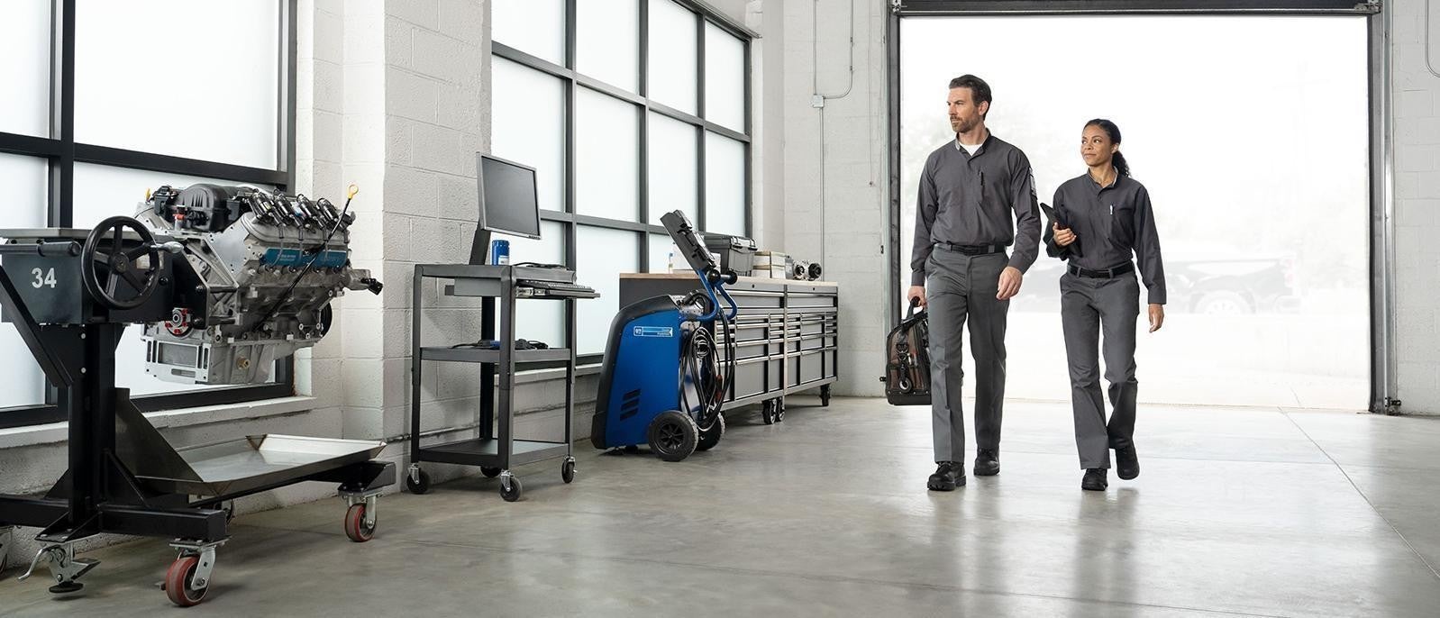 2 certified maintenance technicians walking through a well-lit GMC service center.